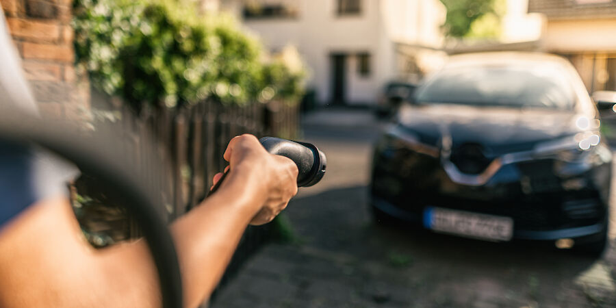 Ein Mann hält ein Ladekabel in der Hand und möchte sein Elektroauto laden.